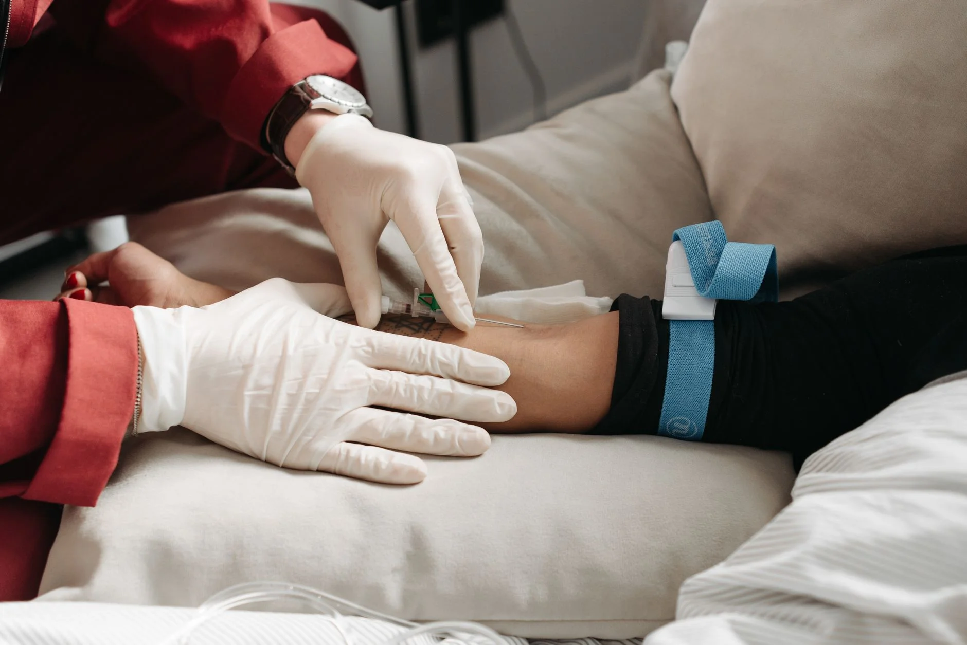 Medical professional in gloves inserting intravenous line into patient's arm in clinic setting. at House of Aetheria, Gurugram