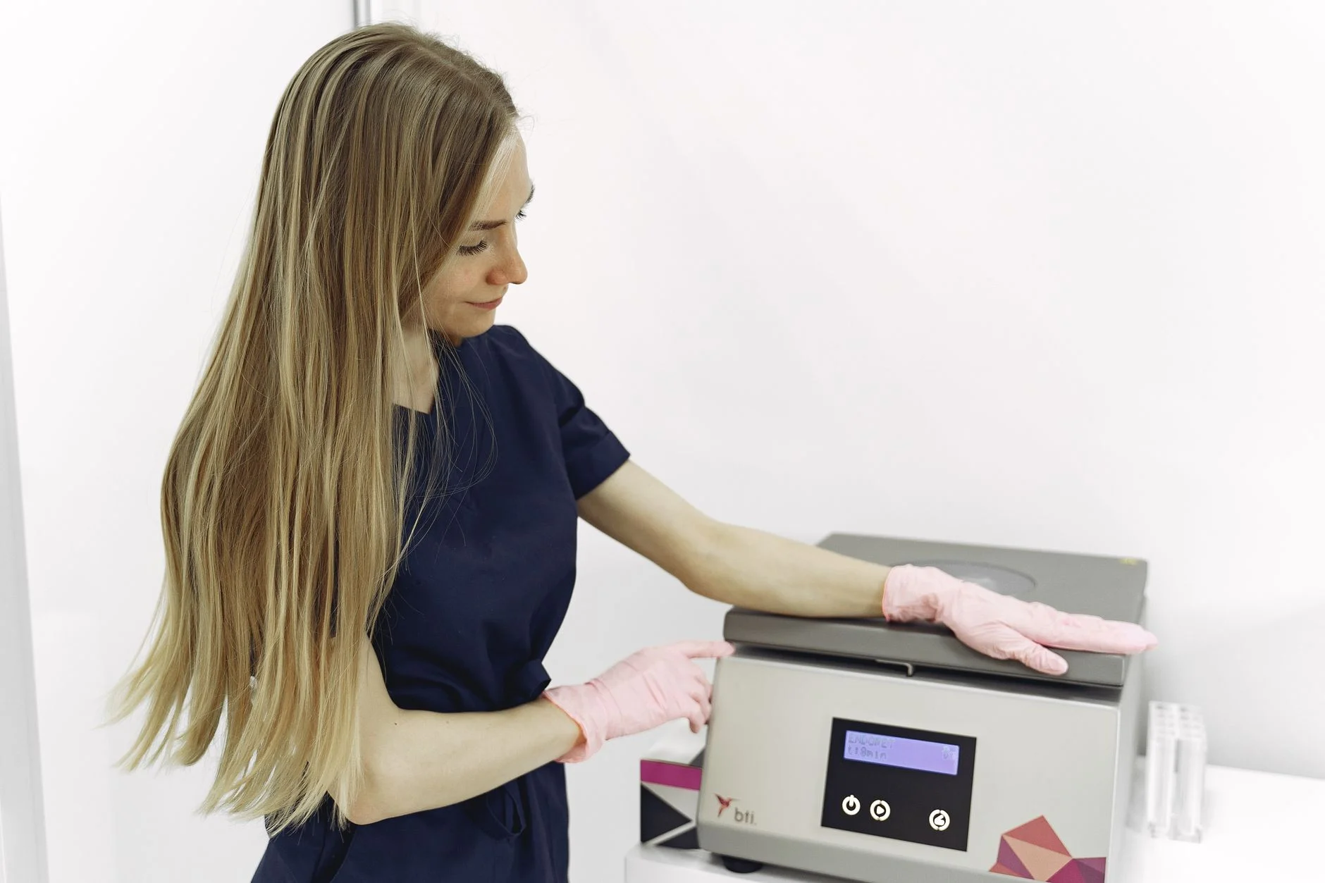 Female medical professional operating laboratory equipment indoors, wearing pink gloves. at House of Aetheria, Gurugram