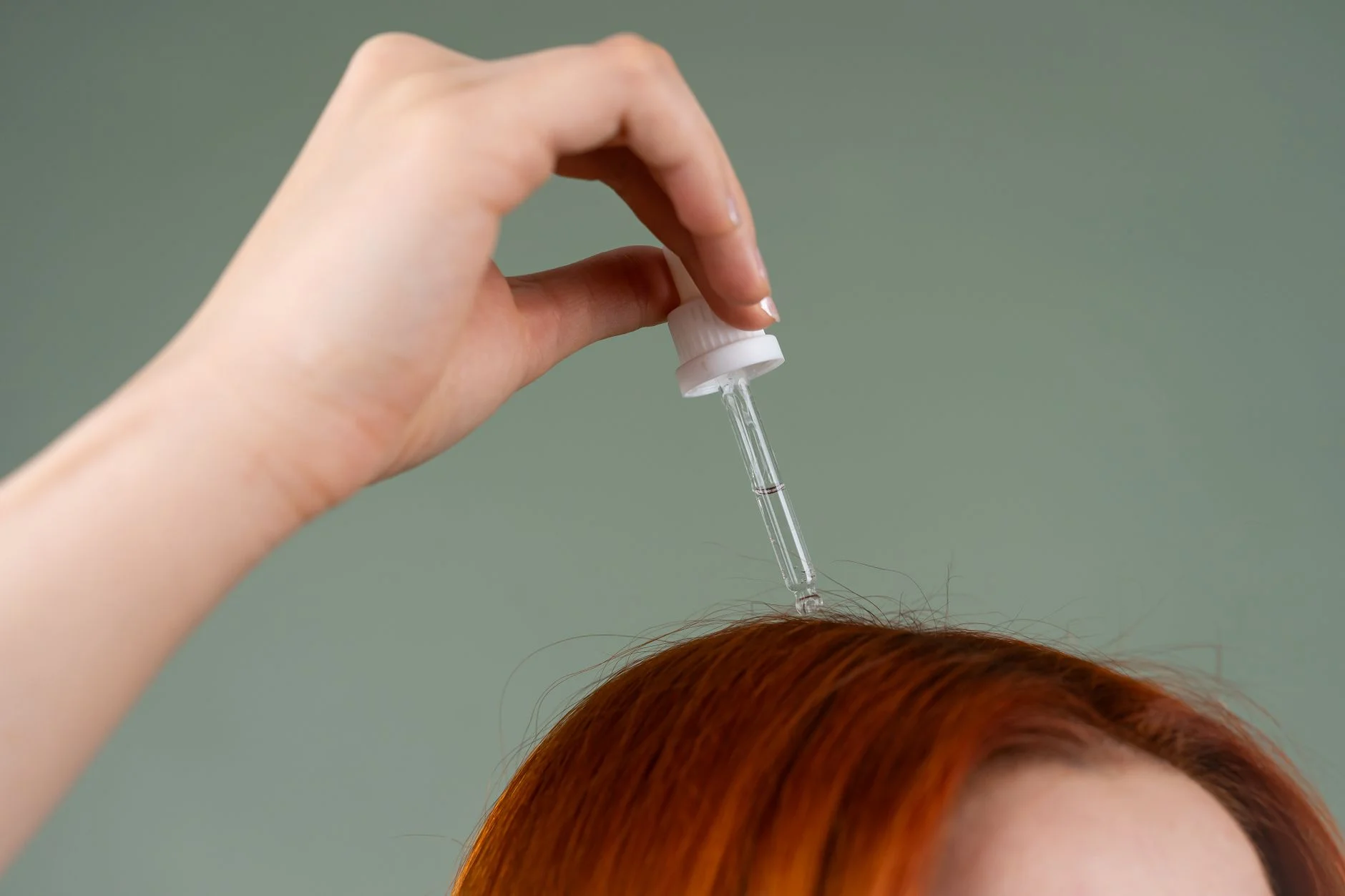 Close-up of hand applying hair serum on red hair with a dropper. at House of Aetheria, Gurugram
